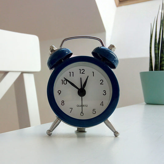 Blue windup alarm clock on a table with a snake plant in a seafoam pot in the background.