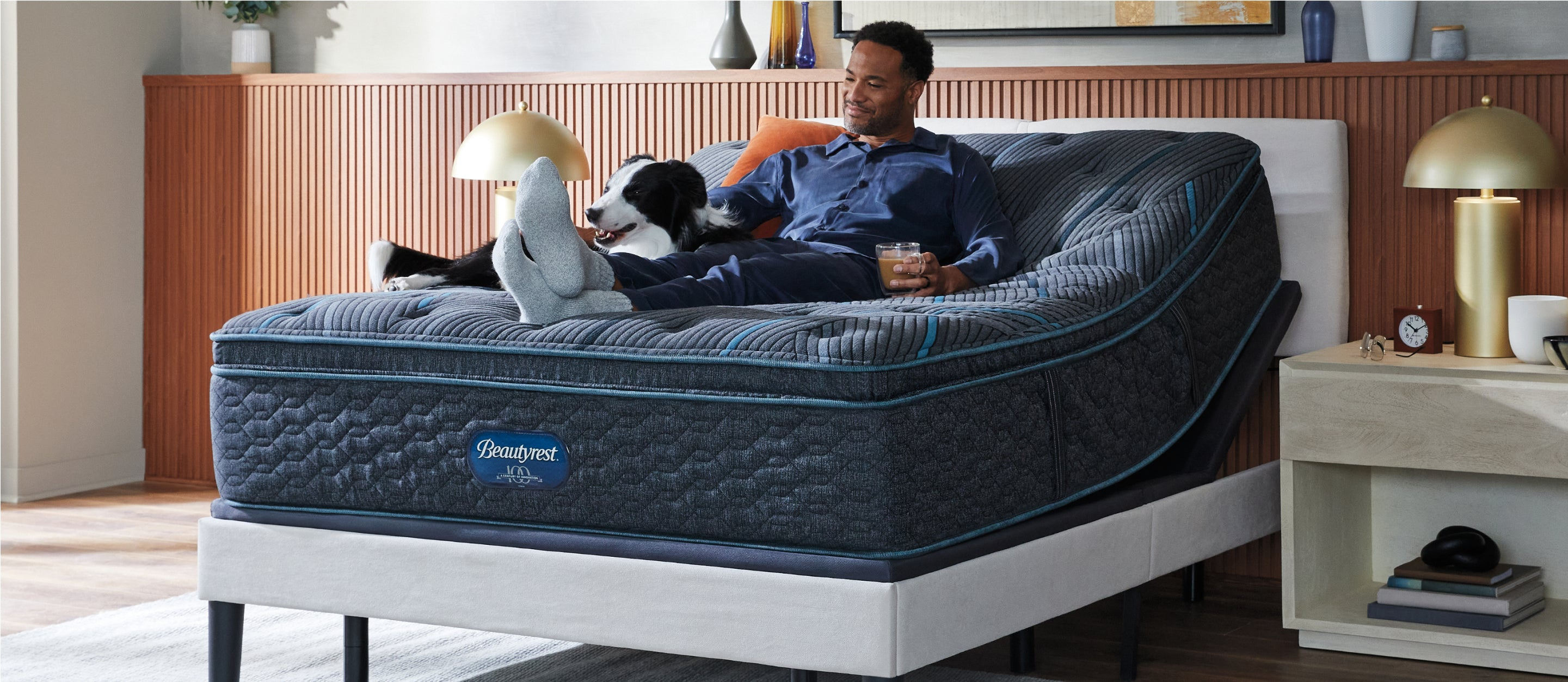 Man with his dog sitting on a Beautyrest mattress slightly elevated on an adjustable base