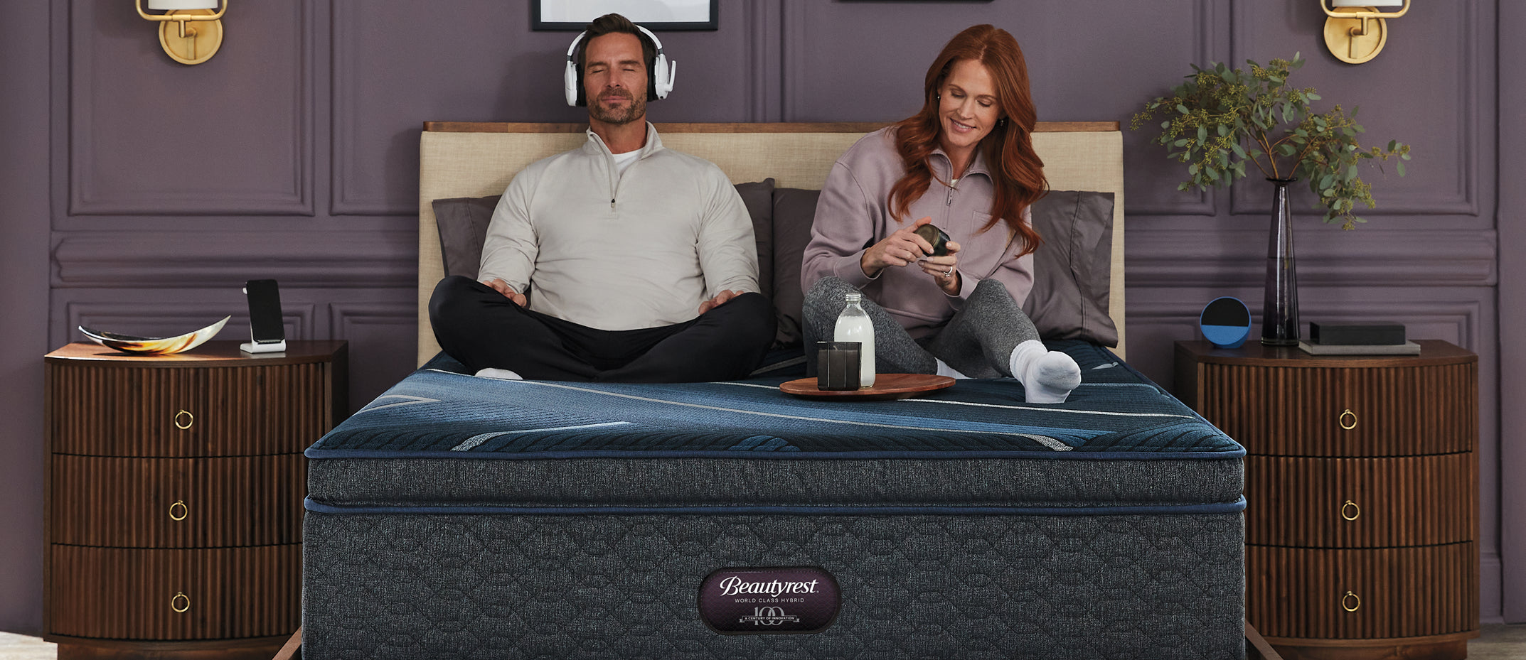 A couple relaxing on a Beautyrest World Class mattress. The man is wearing headphones and the woman is on her phone.