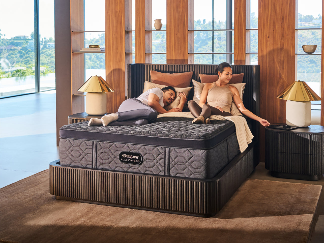 Man laying asleep and woman sitting upright on a Beautyrest Black Hybrid mattress sitting in a dark green bedframe