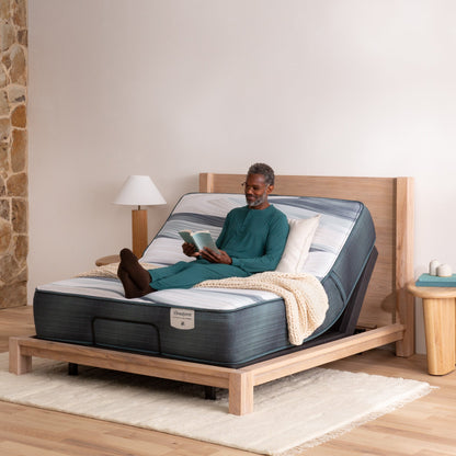 A man sitting on the Beautyrest Advanced Motion adjustable base wearing glasses, reading a book 