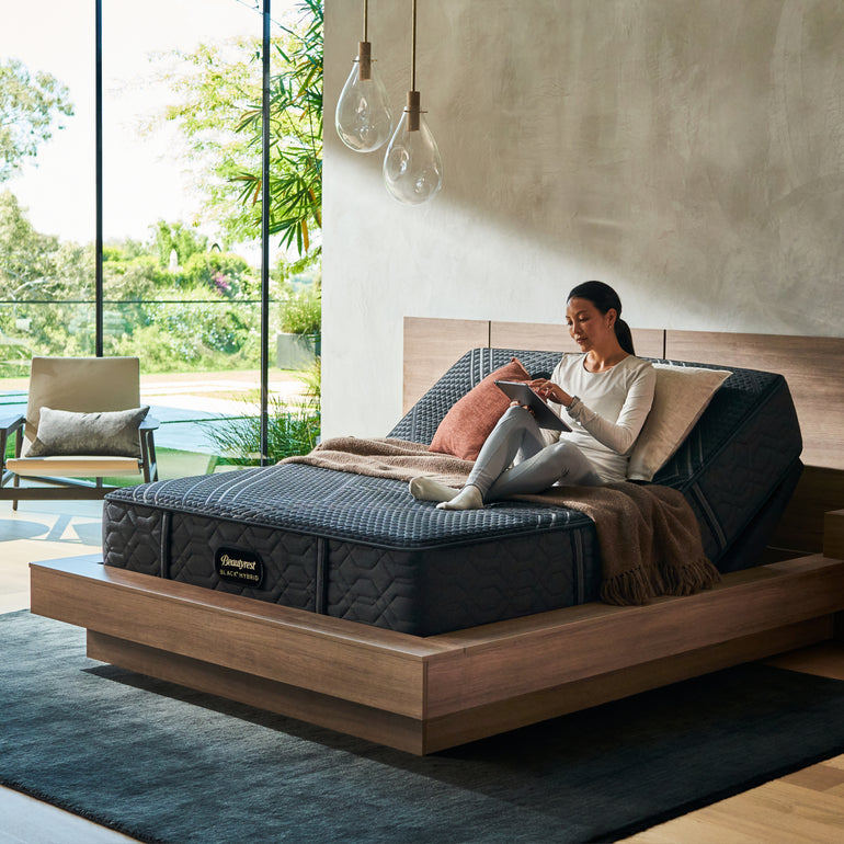 Woman sitting on BeautyRest Firm Hybrid mattress sitting on an adjustable base || series: Series One || feel: Firm