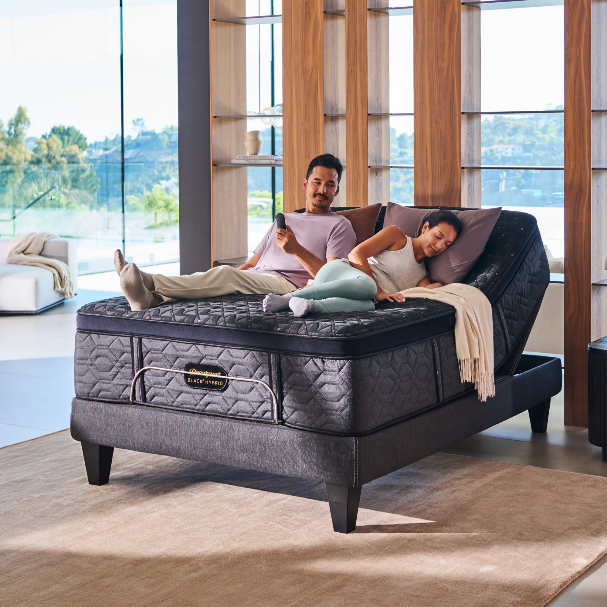 A man and woman laying on a BeautyRest Firm Apex Top Hybrid mattress sitting on an adjustable base || series: Series Four || feel: Firm Apex Top
