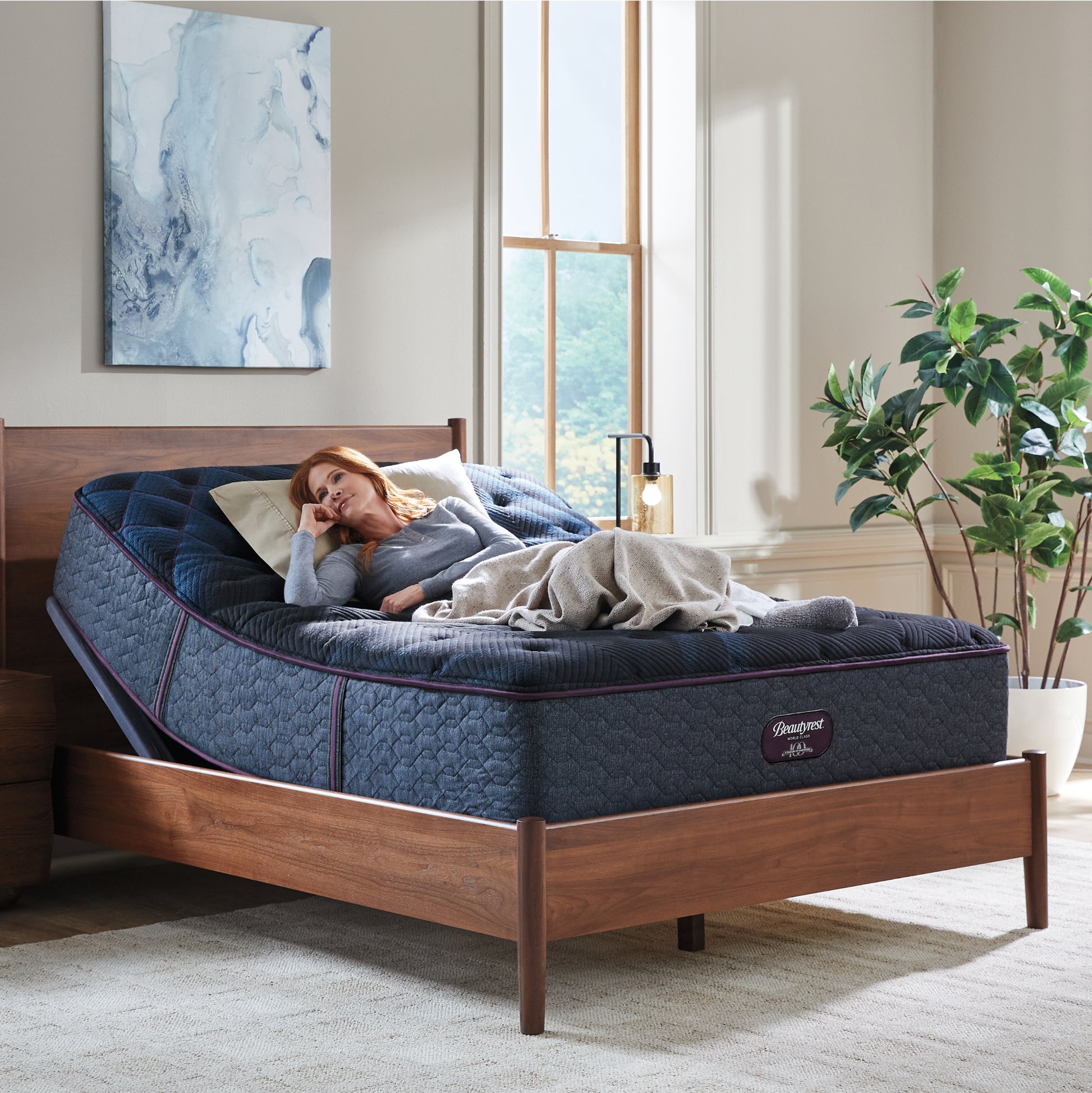 Woman laying on a Beautyrest World Class mattress on and adjustable base siting in a brown bed frame.