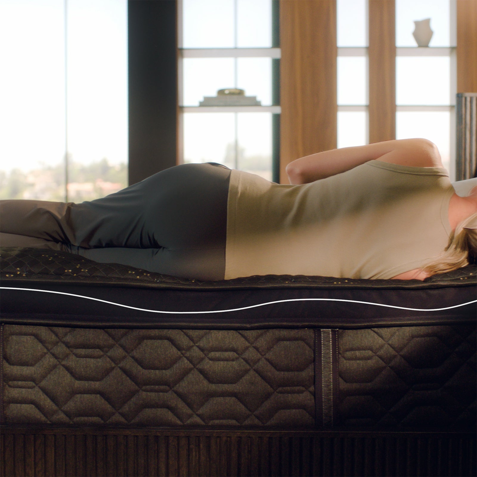 A woman lying on her side on a Beautyrest Black mattress, with a curved line illustration showing proper spinal alignment, emphasizing the body-contouring memory foam for pressure relief and support.