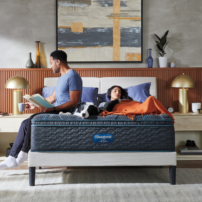 Man sitting on the left side, dog laying in the middle and woman laying on the right side of a Beautyrest Innerspring mattress