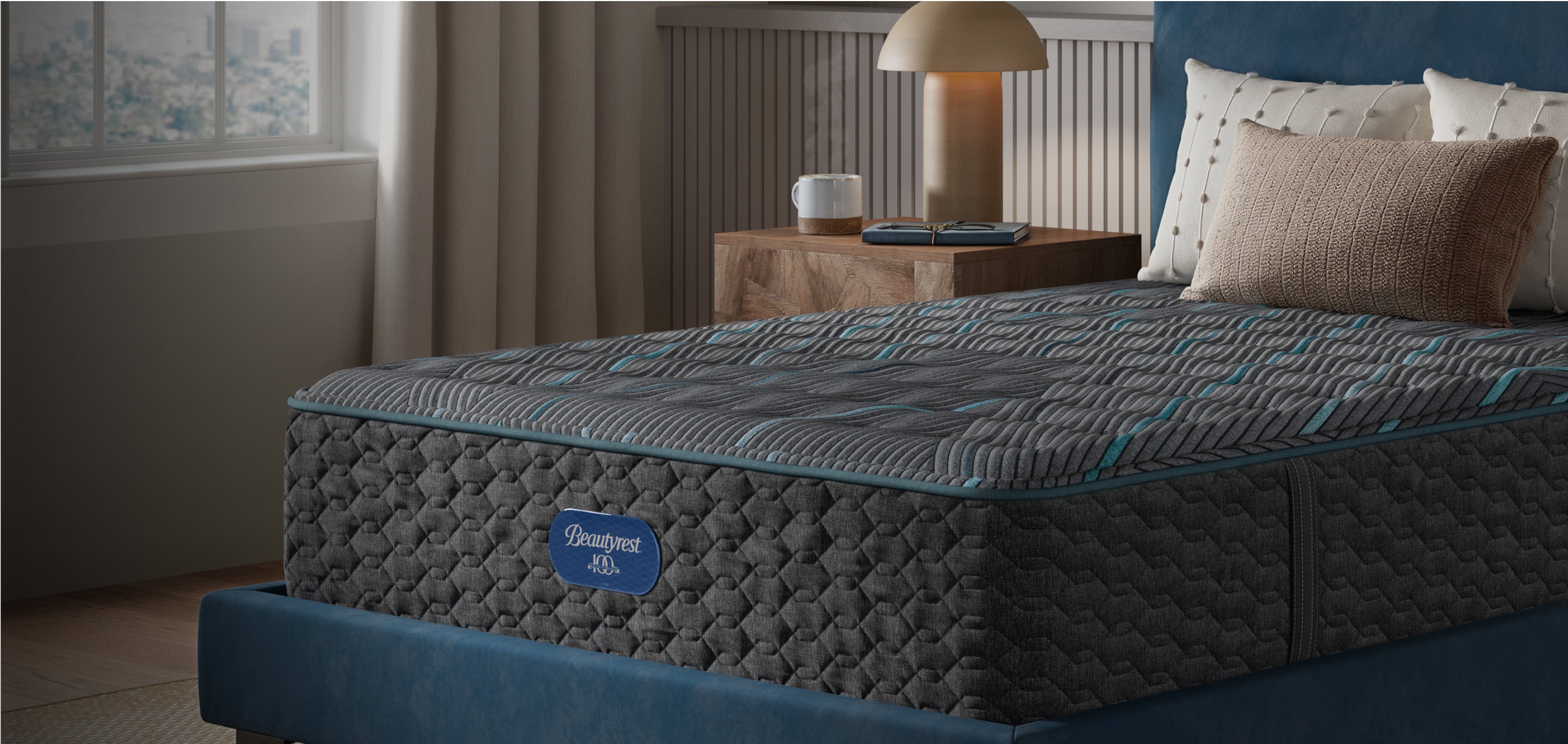 Beautyrest Hybrid mattress sitting in a beige bed frame with 3 pillows and a blanket on top of it.