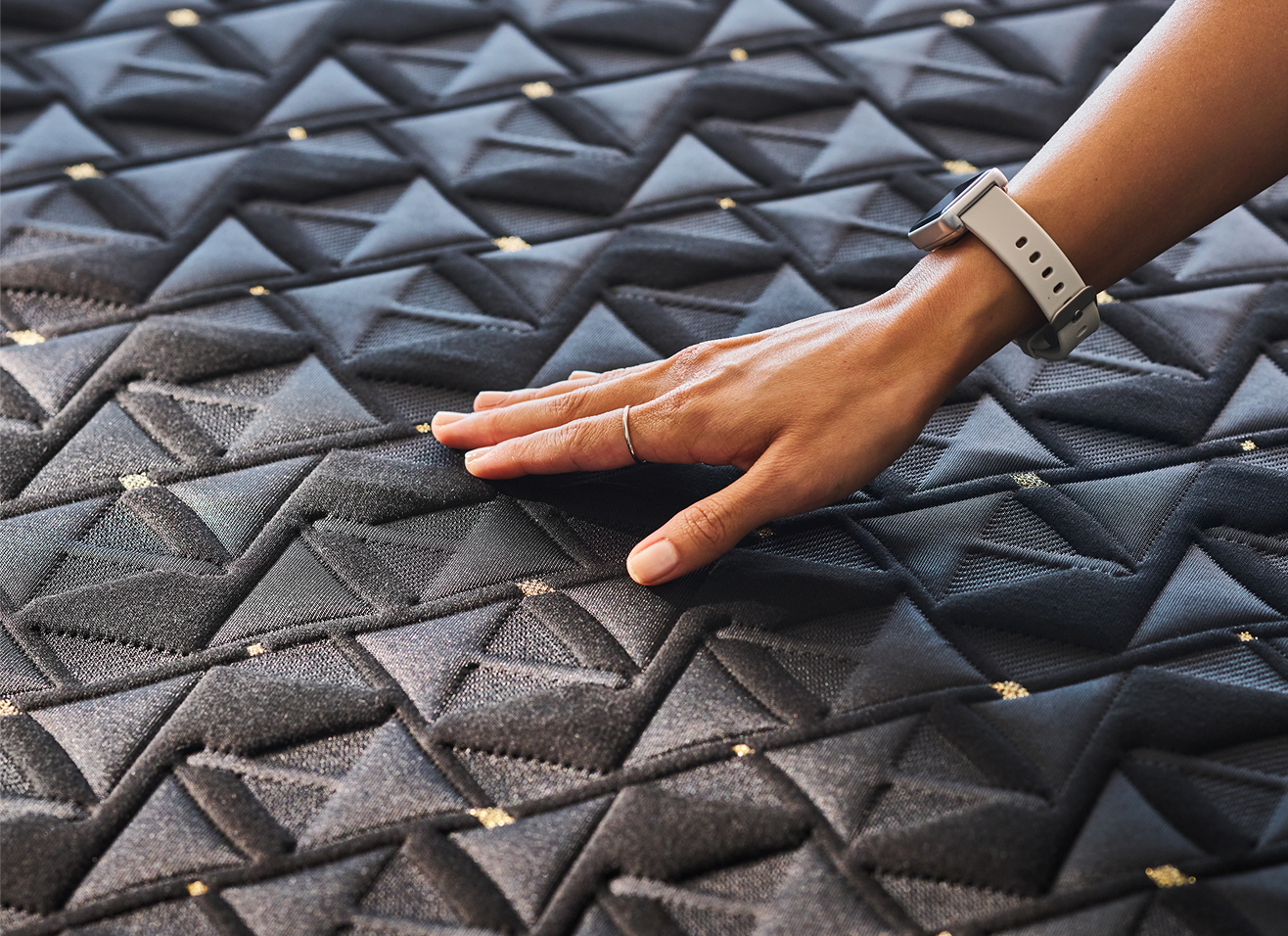 A hand pressing into a hybrid mattress with a smooth black quilted surface and subtle diamond stitching