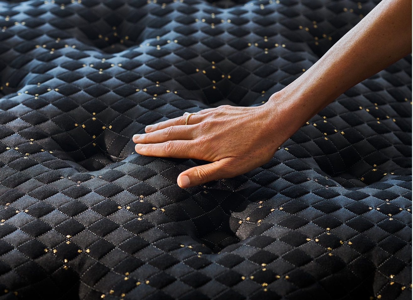 A hand pressing into a quilted innerspring mattress with textured fabric and purple stitching