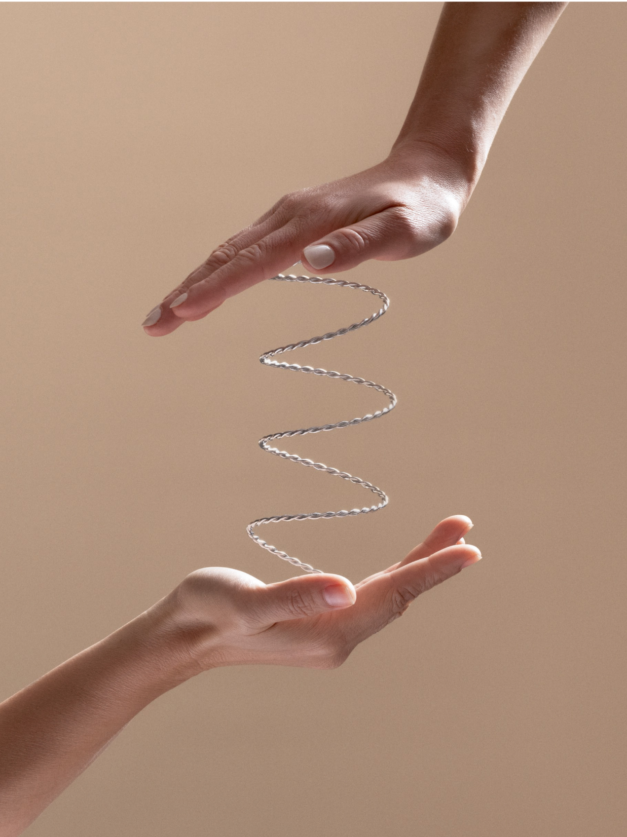 Two hands gently holding a floating, twisted metal coil, symbolizing balance, support, and flexibility against a neutral beige background.