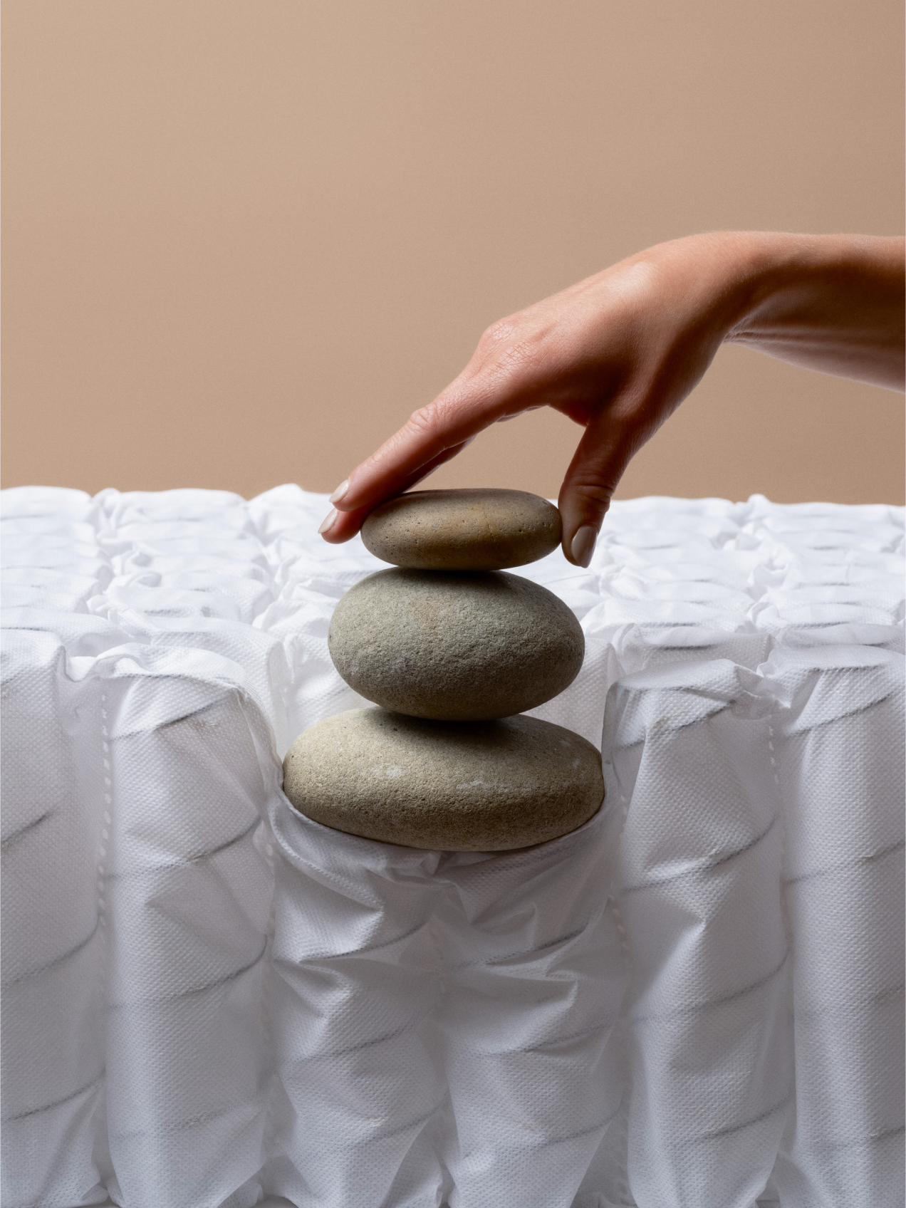 A hand carefully balancing three smooth stones on top of a layer of individually wrapped mattress coils, symbolizing stability, balance, and support.